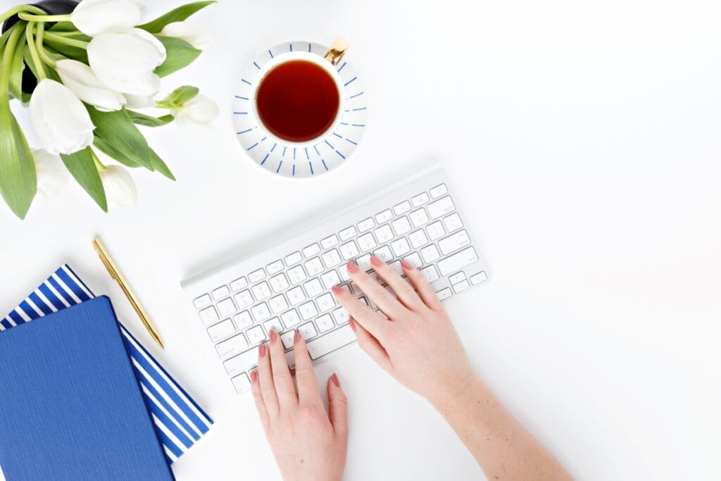 Woman typing on keyboard next to a cup of tea