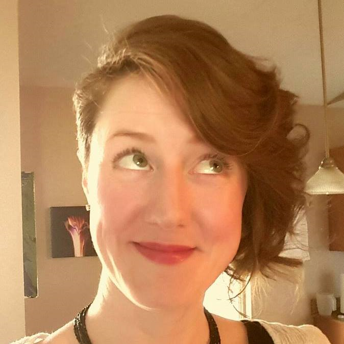 A woman in a home kitchen looking up at the camera.